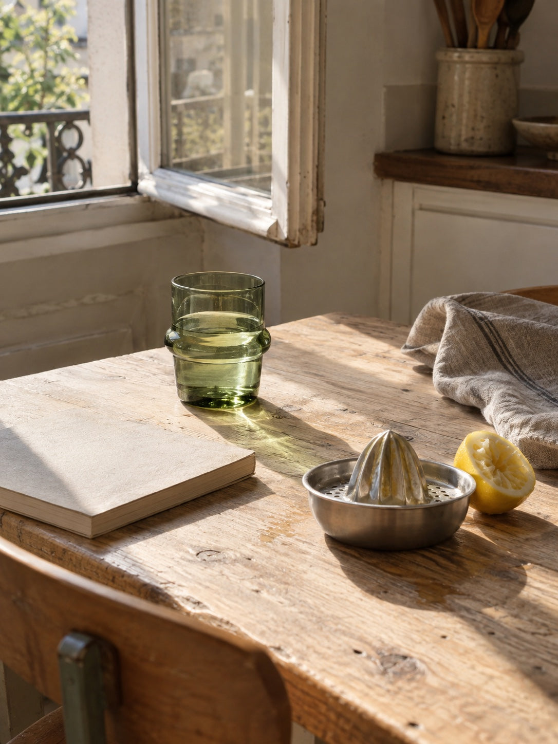 a green glass, a citrus squeezer and a book on a sunlit kitchen table