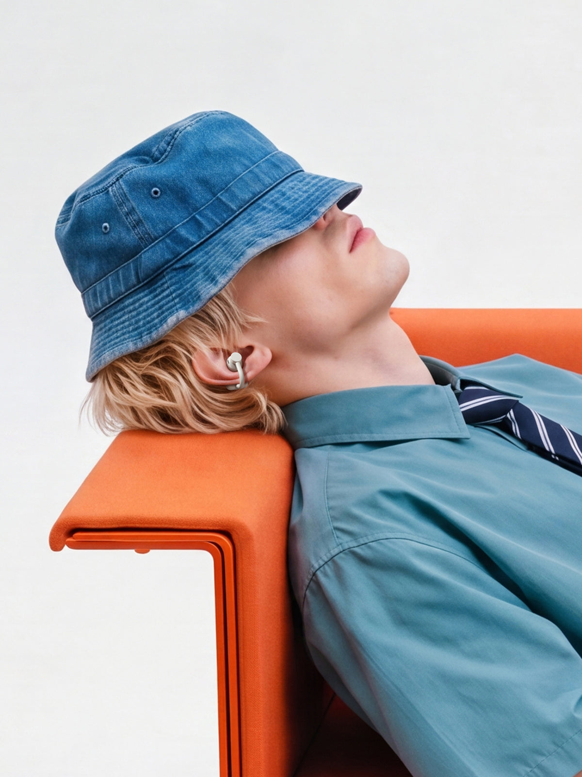 A man in a bucket hat reclining against an orange chair with a Light Grey clip earbud visible