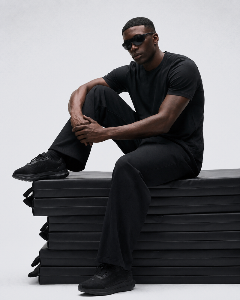 Model seated on stacked mats in the Black Relaxed Tee and black trousers.