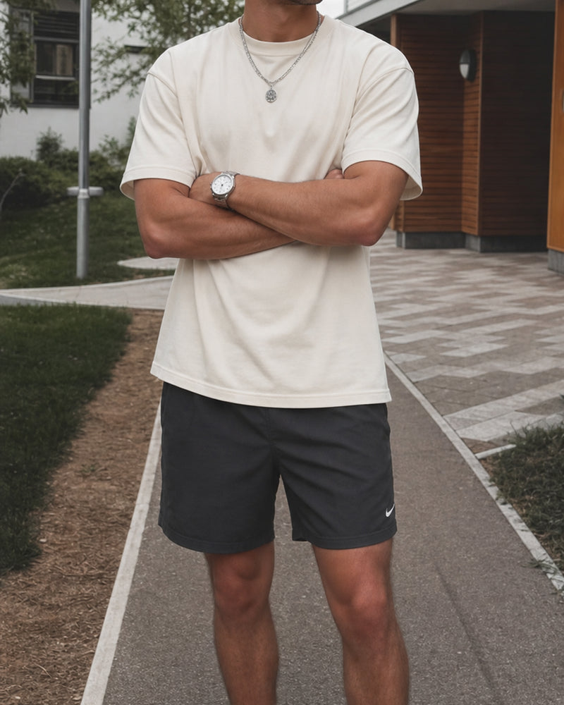 Model wearing an ivory relaxed tee and dark shorts, standing outdoors with arms crossed.