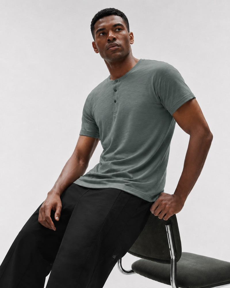 Model leaning against a chair in the Bamboo green Henley.