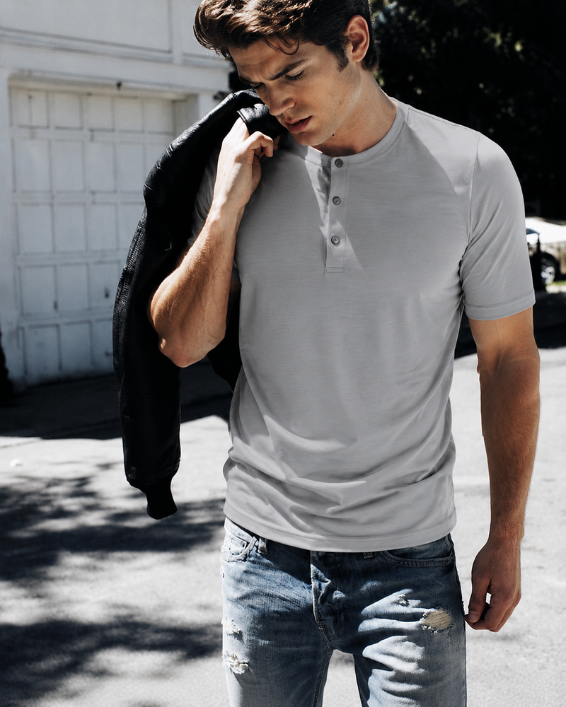 Model wearing a light grey snap-neck Henley with jeans, carrying a jacket over one shoulder.